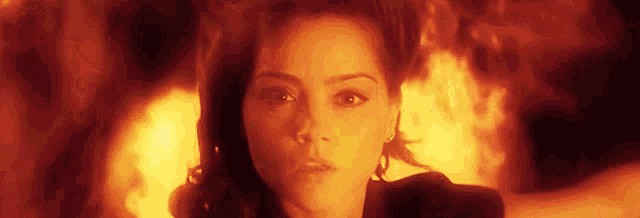 a close up of a woman 's face with a fire in the background .