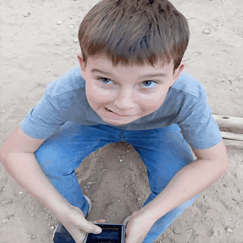 a young boy sitting on the ground holding a cell phone with a screen that says ' samsung ' on it