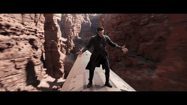 a man in a trench coat is standing on a train in the middle of a canyon
