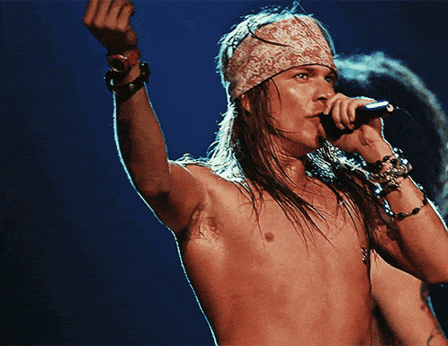 a shirtless man singing into a microphone wearing a bandana