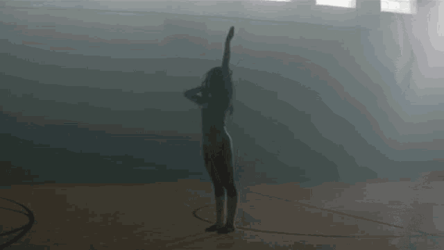 a naked woman is standing in a dark room with her arms up .