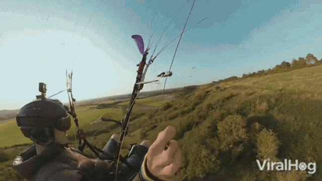 a man is flying a parachute over a grassy hillside and the words viralhog are on the bottom right