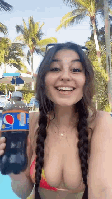 a woman in a bikini is holding a bottle of pepsi in front of a pool .