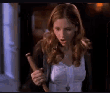 a woman in a white shirt is holding a wooden stick