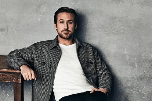 a man wearing a plaid jacket and a white t-shirt is leaning on a wooden table