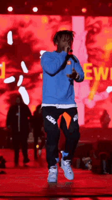 a man is singing into a microphone on a stage while wearing a blue sweater and black pants .