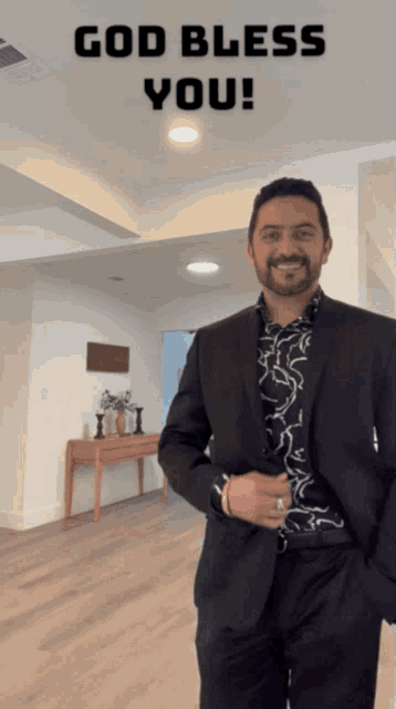 a man in a suit is standing in a room with the words god bless you behind him