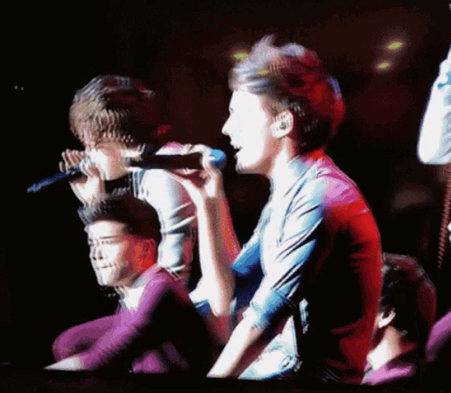a man is singing into a microphone while another man looks on