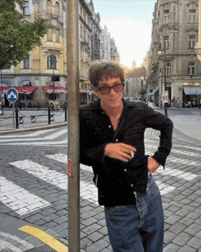 a man wearing sunglasses leans against a pole on a street corner