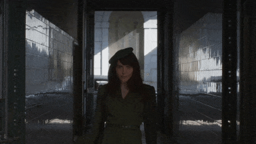 a woman in a green uniform and hat stands in a hallway