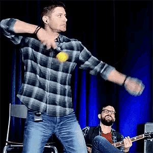 a man in a plaid shirt is throwing a ball while another man plays a guitar