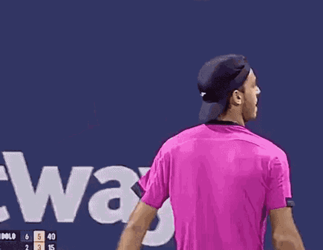 a man wearing a pink shirt and a hat is smiling and touching his hair .