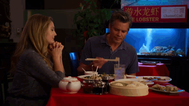 a man and a woman are sitting at a table in front of a lobster tank