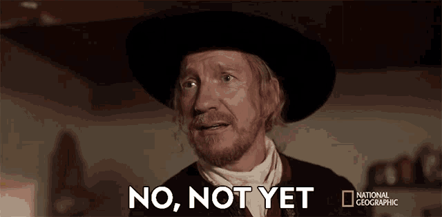 a man with a beard wearing a hat and a scarf is saying no , not yet .