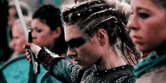 a woman with braids is holding a sword in front of a group of other women .