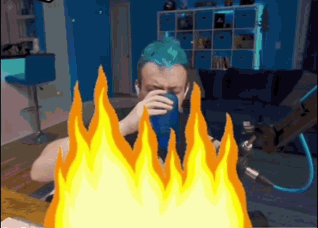 a man with blue hair is drinking from a blue cup with flames surrounding him