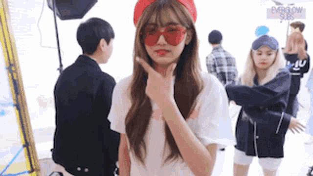 a girl wearing red sunglasses and a red headband is standing in front of a group of people .