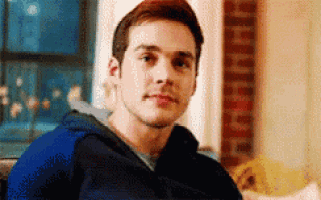 a young man in a blue hoodie is sitting in front of a window in a living room .