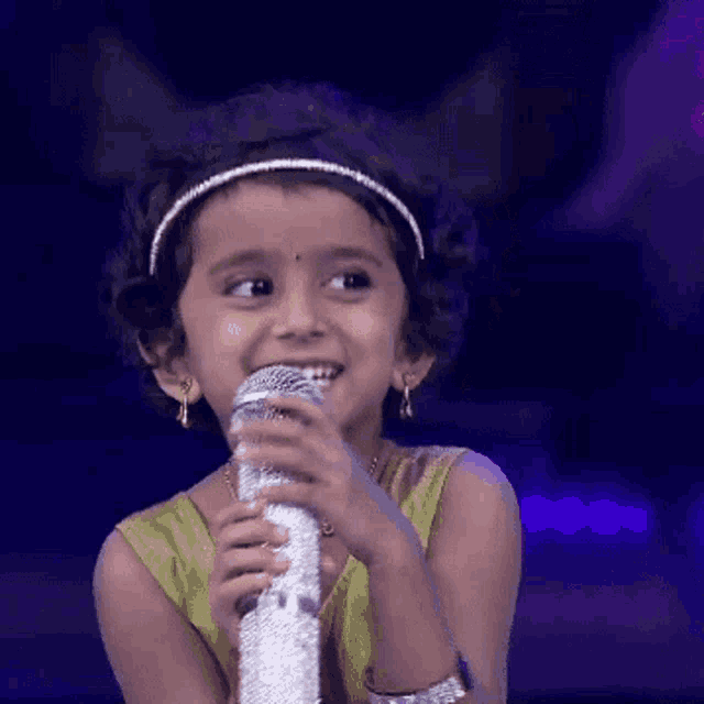 a little girl is holding a microphone in her hand and smiling