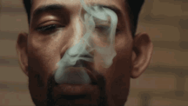 a man with a beard is smoking a cigarette with smoke coming out of his mouth