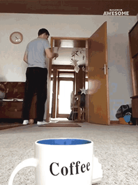 a man standing in a living room next to a cup that says coffee