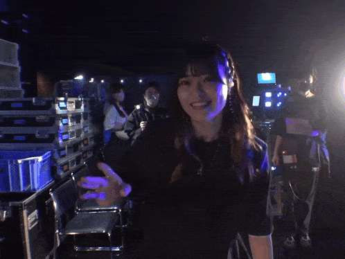 a woman in a black shirt is smiling and waving at the camera