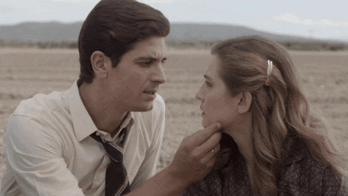 a man in a tie touches a woman 's neck in a field