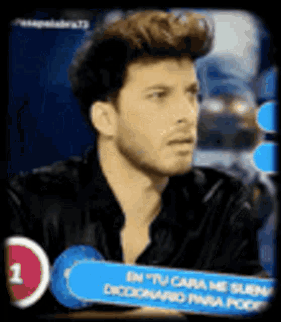 a man in a black shirt is sitting in front of a screen with a sign that says en tu cara me suena .
