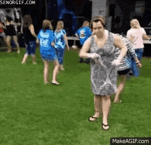 a woman in a dress is standing in the grass with a bottle of water in her hand .