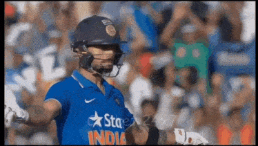a cricket player wearing a helmet and a blue shirt with the word india on it .