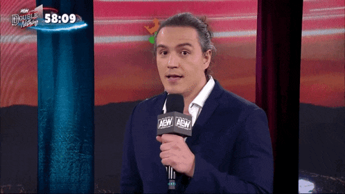 a man in a suit holds a microphone that says aew