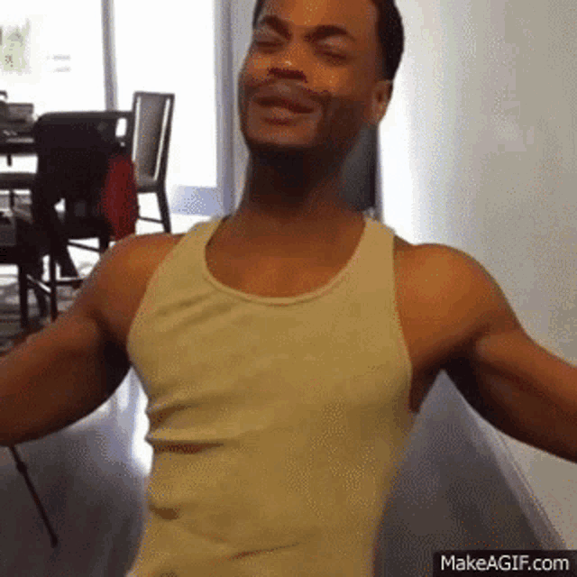 a man in a tank top is standing in a hallway with his arms outstretched and smiling .
