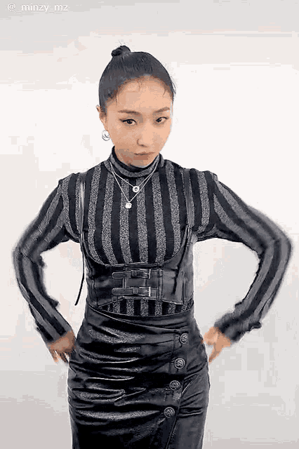 a woman wearing a striped shirt and a black leather skirt is standing with her hands on her hips .