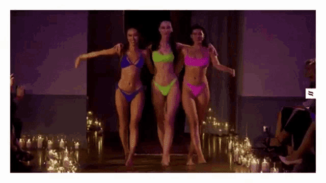a group of three women in bikinis are walking down a runway at a fashion show .