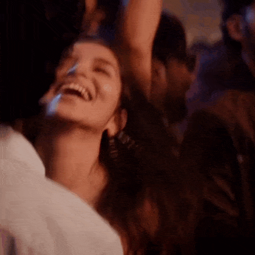 a woman is laughing in a crowd of people at a party with her arms in the air .