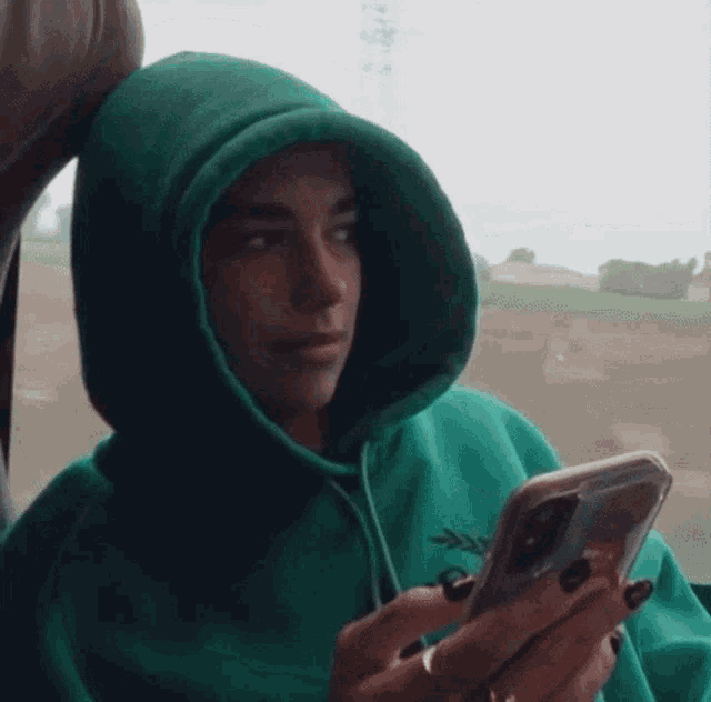 a woman in a green hoodie holds a cell phone