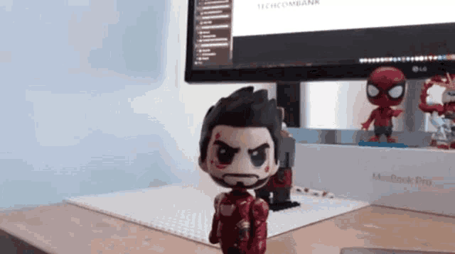a figurine of iron man is sitting on a desk in front of a macbook pro