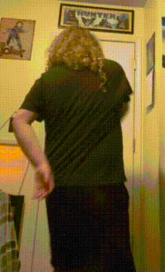 a man in a black shirt is standing in a room with a metallica poster on the wall behind him
