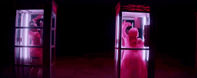 a woman in a pink dress is dancing in a pink phone booth .