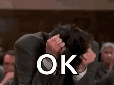 a man in a suit is covering his face with his hands and the word ok is written on the screen .