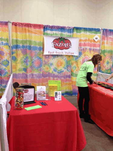 a woman in a green shirt stands in front of a table with a banner that says fazoli 's fast fresh italian