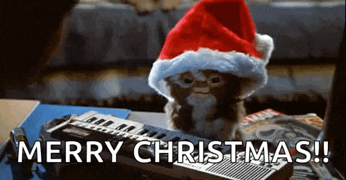 a gremlin wearing a santa hat is sitting on top of a keyboard .
