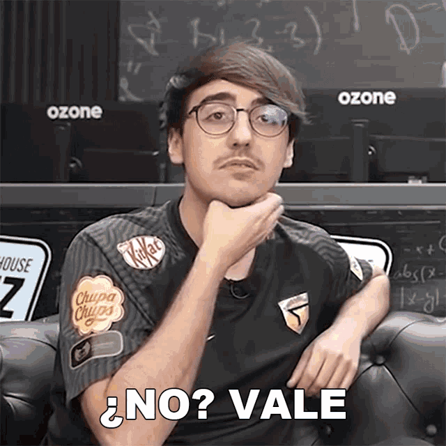 a man with glasses and a chupa chups shirt is sitting on a couch