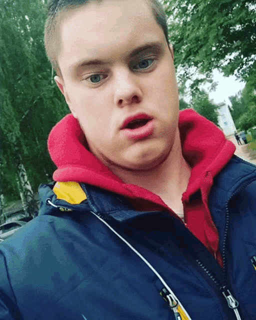 a young man wearing a blue jacket and a red hoodie is making a surprised face