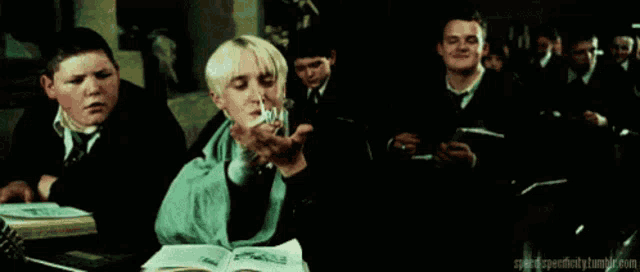 a group of boys are sitting at a table in a classroom and one of them is holding a book .