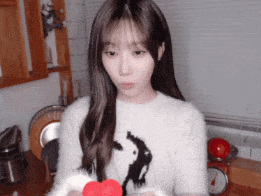 a girl in a white sweater holds a red heart in her hand