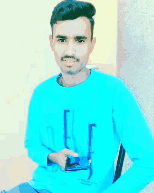 a young man is sitting in a chair holding a cell phone and pointing at it .