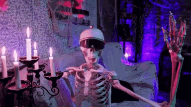 a skeleton is sitting on a bed with candles in a room with purple lights .