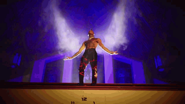 a man is standing on a stage with his arms outstretched in front of a wall that says 12
