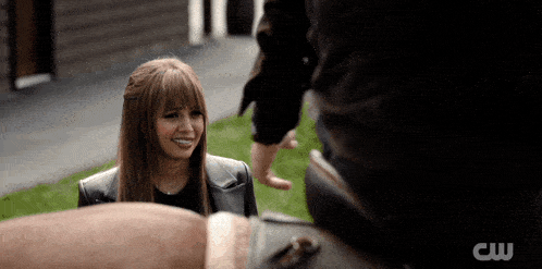 a woman in a leather jacket is smiling while talking to a man with a cw logo in the corner